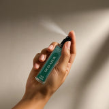 Hand holding a Zour Oud Azur perfume bottle with a spray being released.