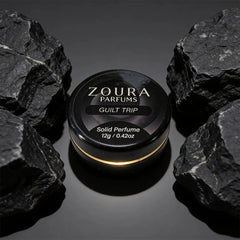 Zoura Guilt Trip Solid Perfume jar between black rocks