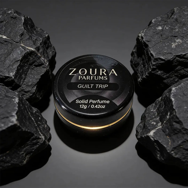 Zoura Guilt Trip Solid Perfume jar between black rocks