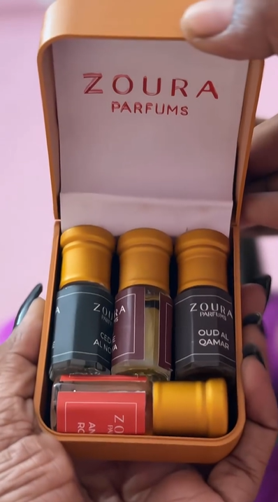 Woman unboxing a Zoura Parfums attar product against a pink backdrop, video review.