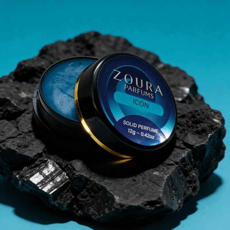 Open jar of Zoura Icon Unisex Solid Perfume resting on black charcoal stone, blue backdrop