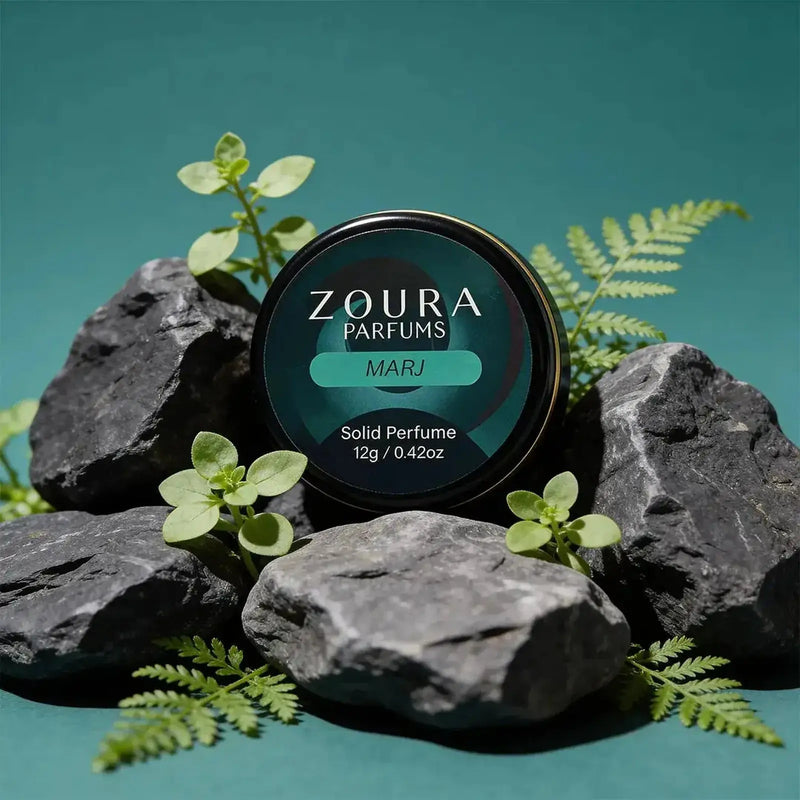 Zoura Marj Unisex Solid Perfume jar surrounded by dark stones and green ferns