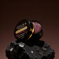 Open jar of Zoura Midnight Brew Unisex Solid Perfume resting on black charcoal stone