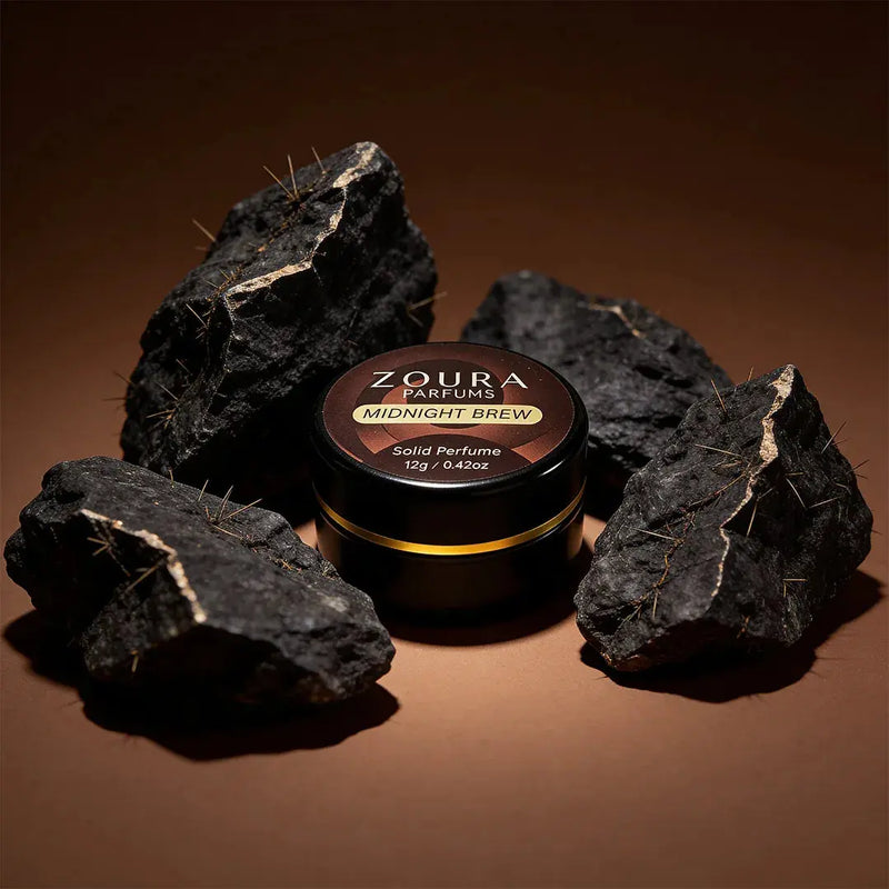 Zoura Midnight Brew Unisex Solid Perfume jar surrounded by gold-veined black rocks