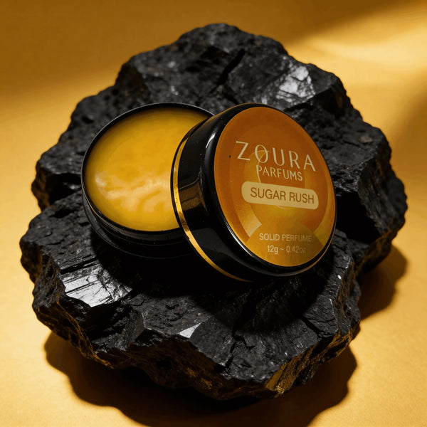 Open jar of Zoura Sugar Rush Unisex Solid Perfume resting on black charcoal stone