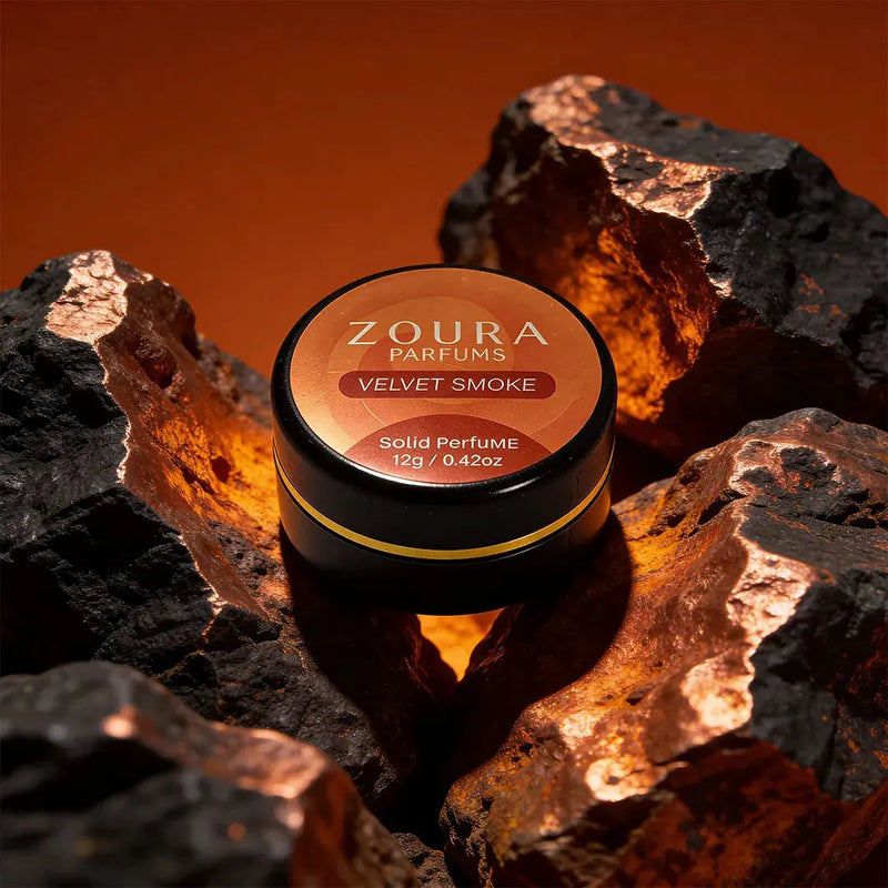 Zoura Velvet Smoke Unisex Solid Perfume jar surrounded by glowing ember-lit rocks