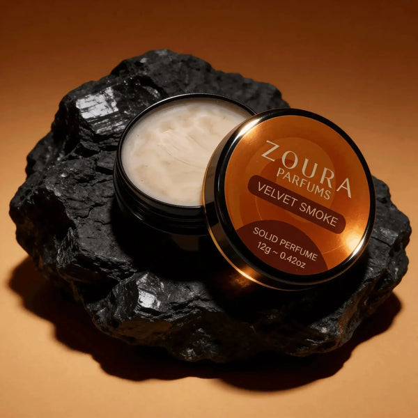Open jar of Zoura Velvet Smoke Unisex Solid Perfume resting on black charcoal ston